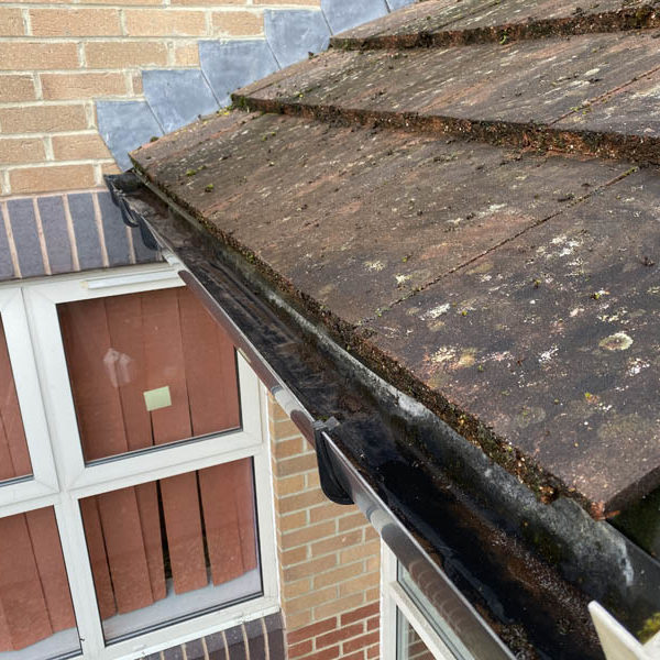 Clear gutter running along a lichen-covered tiled roof on a brick house