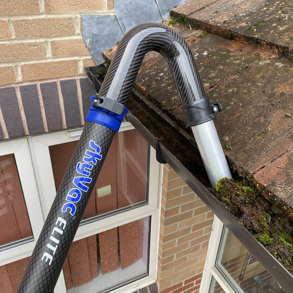 SkyVac Elite carbon fibre pole reaching into a moss-filled gutter on a brick house