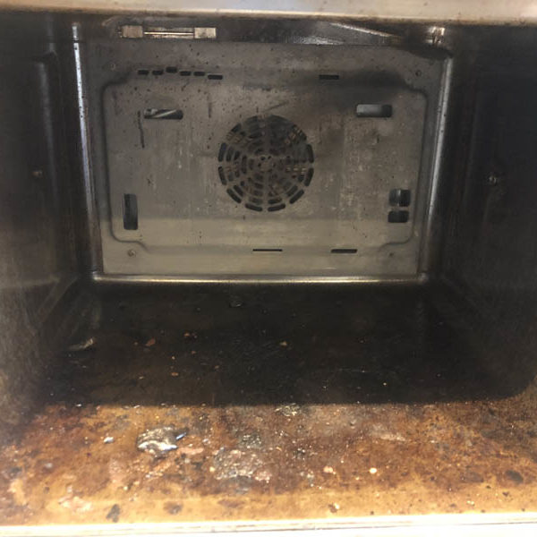 Oven interior with heavy burnt-on carbon deposits across the base and stained walls
