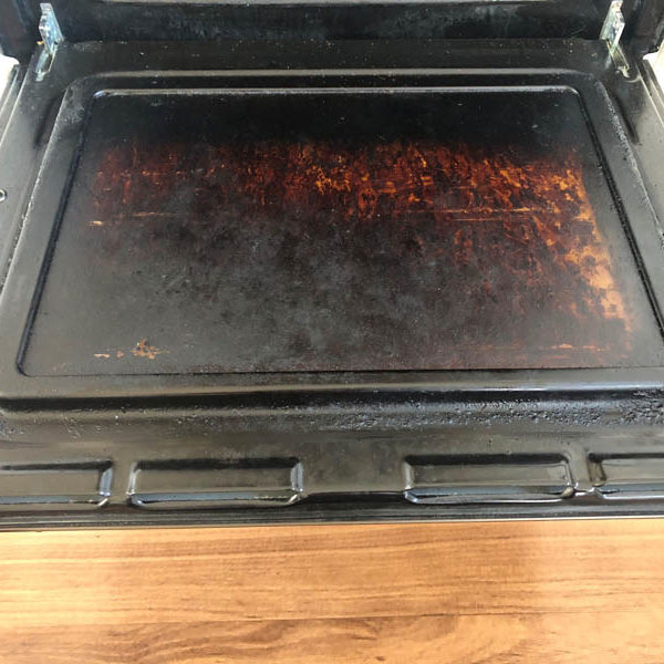 Open oven door with the inner glass and frame coated in thick burnt-on grease