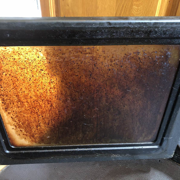 Oven door glass heavily stained with baked-on brown grease and carbon deposits