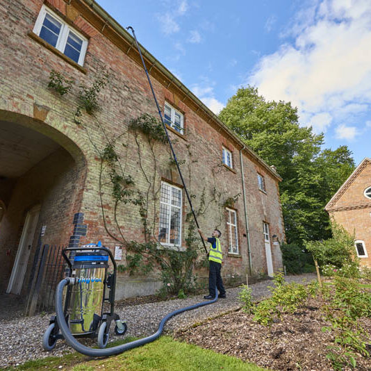 Operative clearing gutters on a brick building with a SkyVac Industrial suction pole