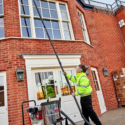 Operative using a SkyVac Interceptor suction pole to clear gutters on a brick building