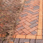 Block paving part-cleaned, showing moss-stained bricks beside bright clean bricks