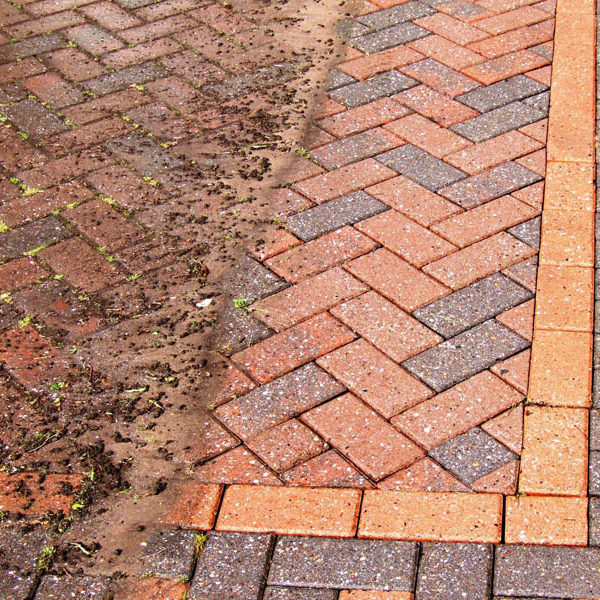 Block paving part-cleaned, showing moss-stained bricks beside bright clean bricks